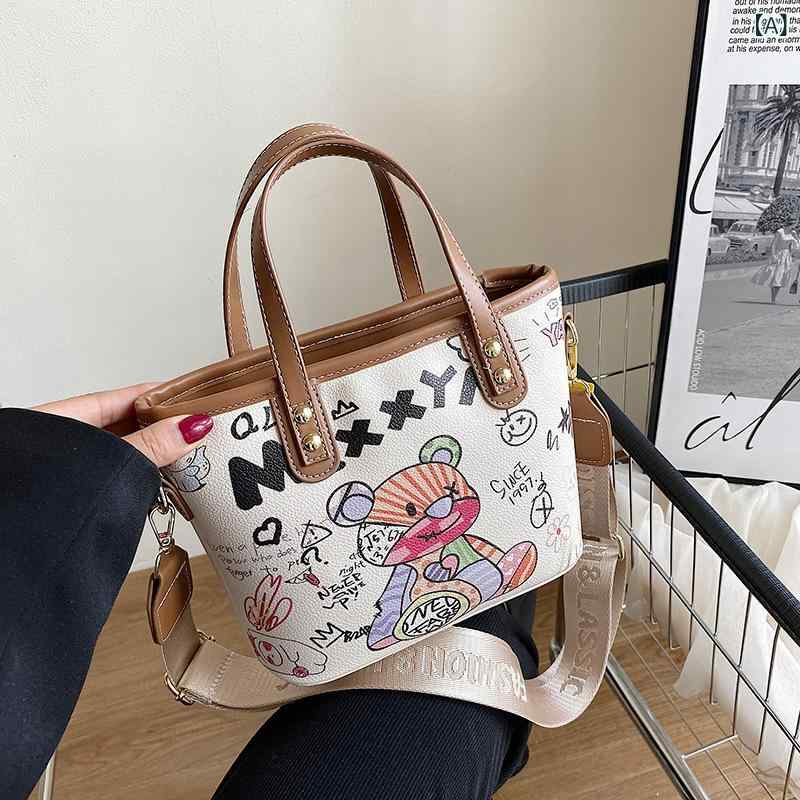 ショルダーバッグ 大容量 女性用 韓国風 トレンド コーデ 万能 個性 グラフィティ デザイン かわいい カートゥーン 水桶型 斜めがけ ミディアム サイズ ブラウン ホワイト カラーバリエーション PU素材 ポリエステル裏地 ステッチ アクセント コン
