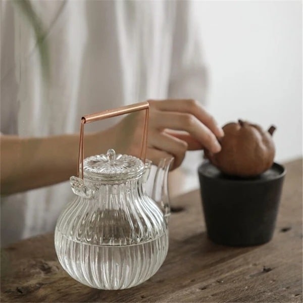 灯し火陶芸コンロ専用に心積もりされた、分かりやすいな耐熱硝子製ティーポット。銅製の手持ち部分が付いています。